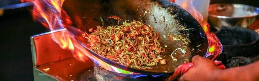 Vibrant close-up of chef cooking noodles in a flaming wok inside a restaurant kitchen.