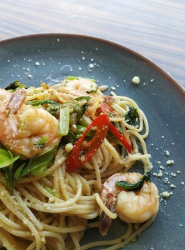 Appetizing shrimp pasta garnished with fresh chili and herbs in a close-up view.